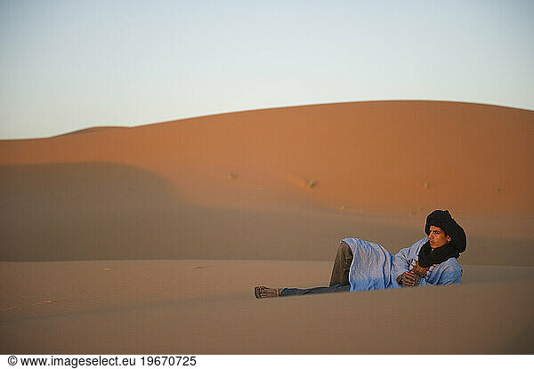 A desert boy sits on the top of a sand dune at sunrise.