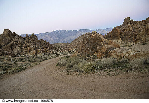 A dirt road winds through a rocky landscape at dawn.