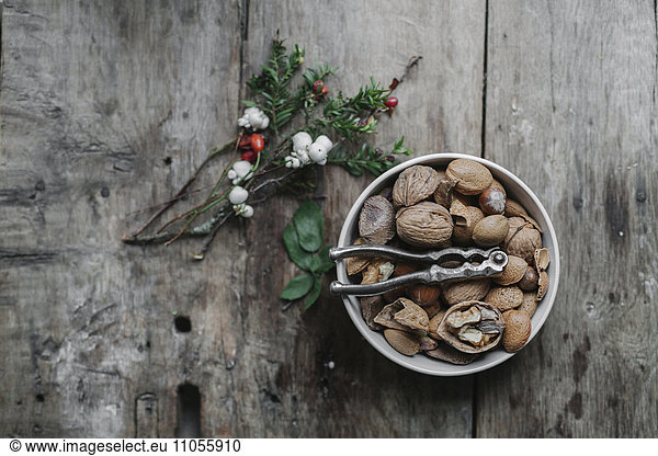 A dish of nuts and a nut cracker on a table with a sprig of yew wit red berries.