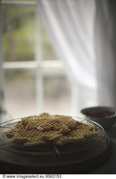 A dish of waffles on a tabletop. Net curtains draped back from a window.
