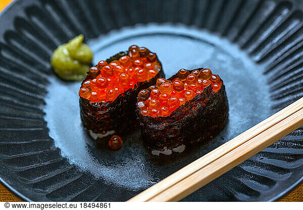 A dish with two portions of sushi  rice wrapped in seaweed with fish roe.