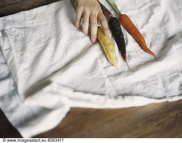 A domestic kitchen table. A person arranging fresh carrots on a white cloth.
