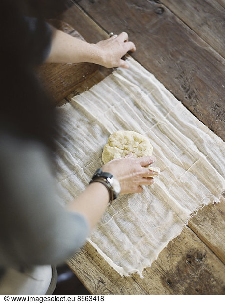 A domestic kitchen table. A view from above of a woman wrapping fresh pastry in a muslin cloth to keep it fresh.