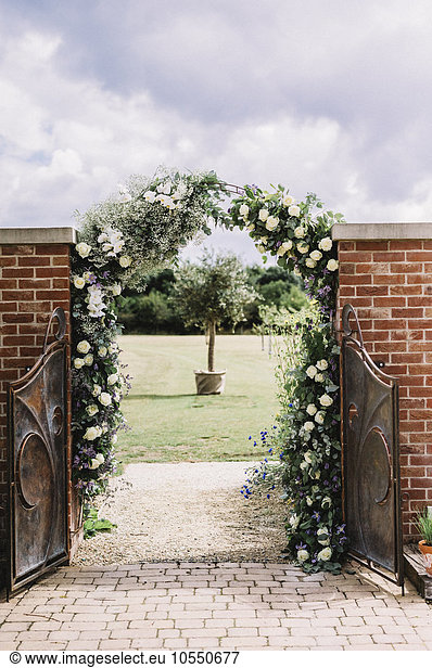 A door in a wall  and a white rose arch in a garden  with a view to a sundial.