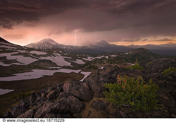 A dramatic flash of lighting compliments the stormy skies at sunset over Oregon's Three Sisters mountains.