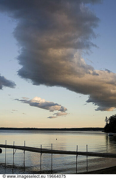A dramatic line of clouds forms in the evening sky over a silhouetted dock as the gentle waves ease to the s