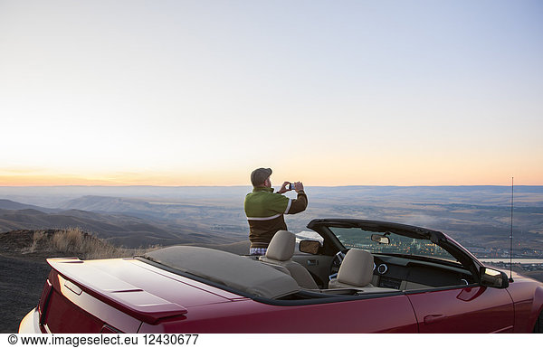 A driver stops to take a photograph at sunset near Lewiston  Idaho  USA on a road trip with his convertible sports car.