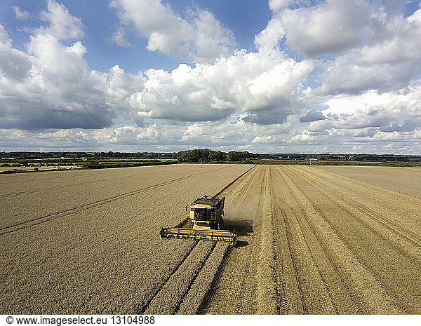 A drone shot of fields in a farming landscape  and a combine harvester working harvesting a crop.