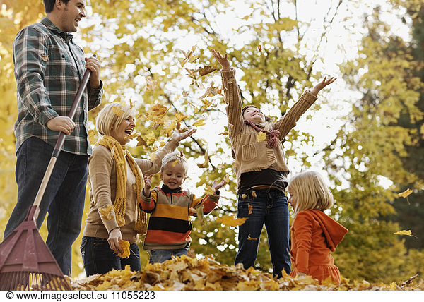 A family  adults and two children playing in autumn leaves.