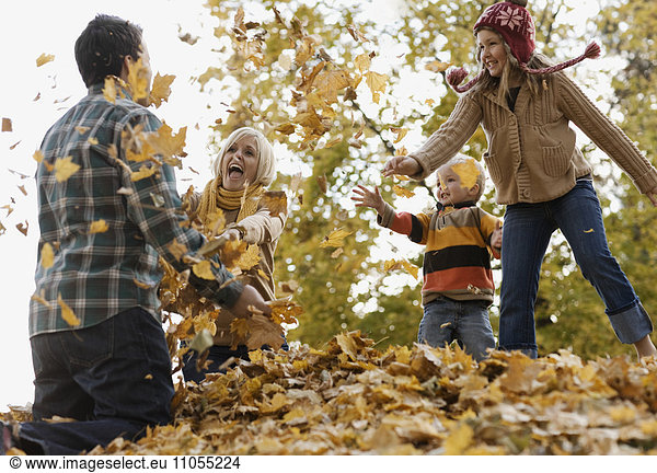 A family  adults and two children playing in autumn leaves.