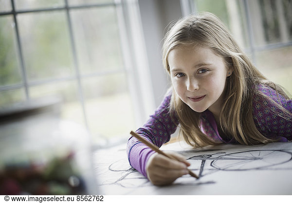 A family home. A child sitting at a table using a pencil and creating a line drawing. Artwork. Drawing.