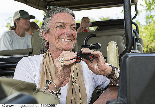 A family in a safari jeep in a wildlife reserve  a senior woman with binoculars.
