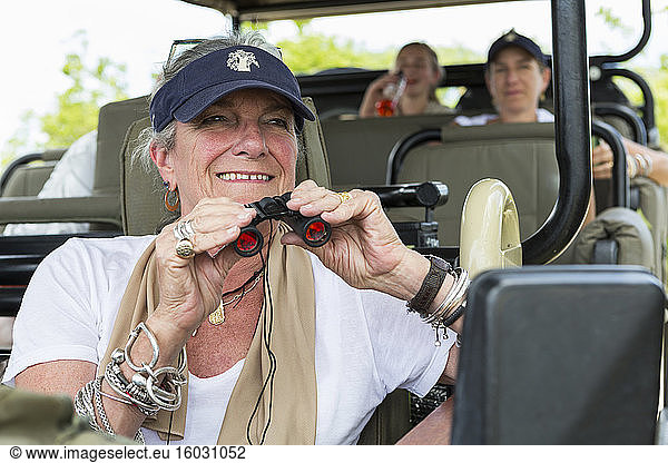 A family in a safari jeep in a wildlife reserve  a senior woman with binoculars.