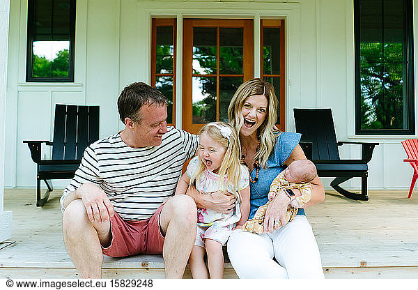 A family of four laughing together while sitting on a modern porch