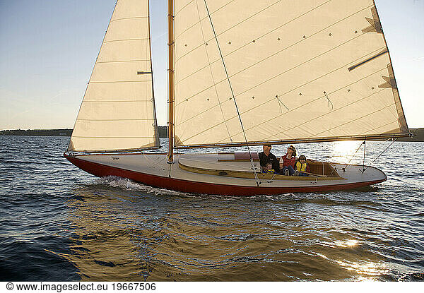 A family of four sail their small red sailboat in the evening sun.