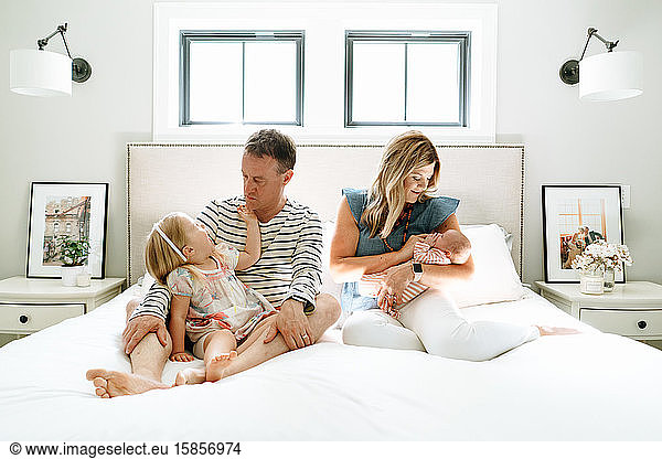 A family of four sitting together in a bright  modern bedroom