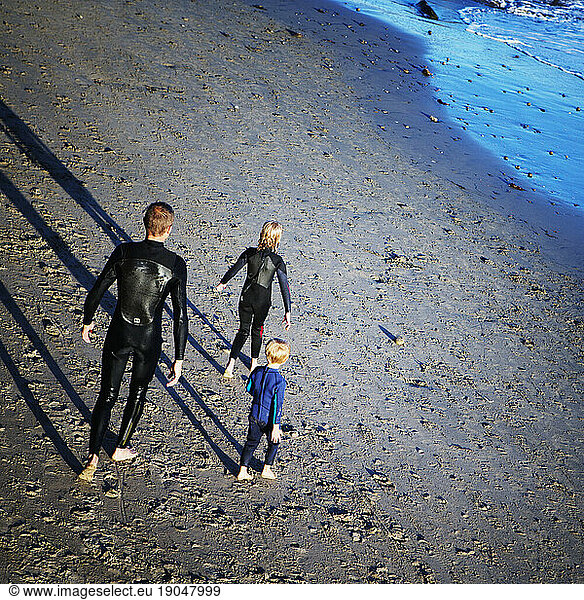 A family on the beach in wet suits.