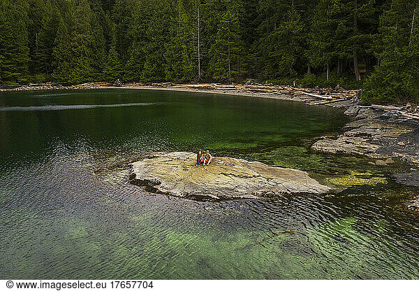 A family sits on rock island surrounded by clear green water and trees