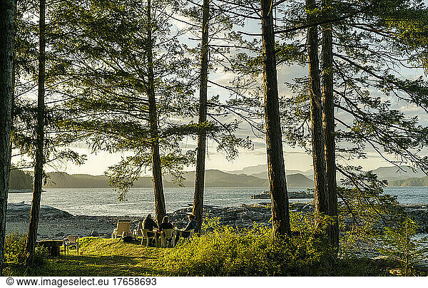 A family sits under trees with big bay and mountains in background