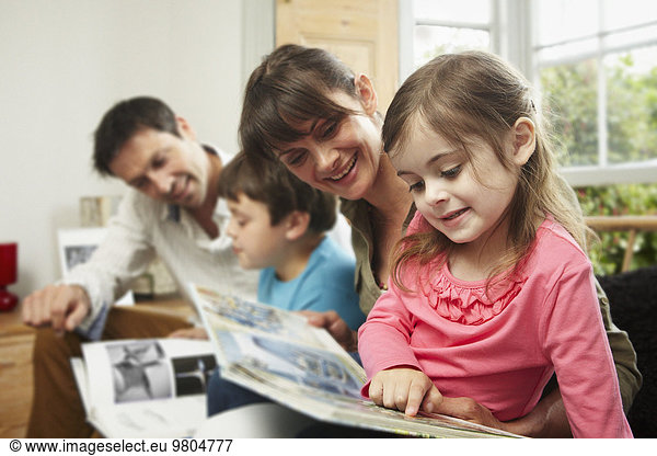 A family  two parents and two children at home  reading together.
