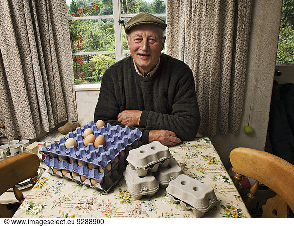 A farmer seated at a table in a farmhouse with trays of fresh eggs.