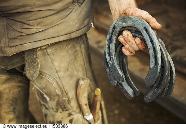 A farrier holding a handful of metal horseshoes.