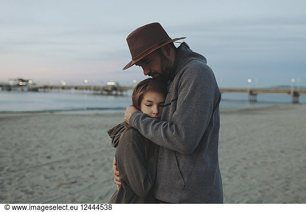 A father and daughter having a tender moment  the father holding his daughter in an embrace on a beach at dusk; Long Beach  California  United States of America