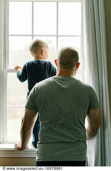 A father and his toddler son looking out of a window together