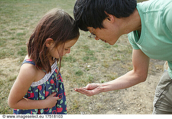 A father and little girl look carefully at something in his hands