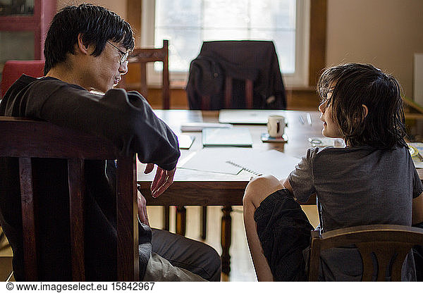 A father and son sit at table in morning light talking together