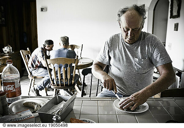 A father cutting a sandwich while his sons eat lunch on the kitchen table in their farm house in Keymar  Maryland.