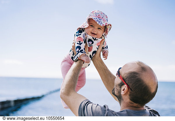 A father lifting his baby daughter in a sun bonnet up in the air