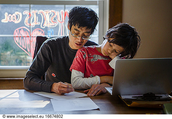 A father works from home at dining table with tween son on his lap