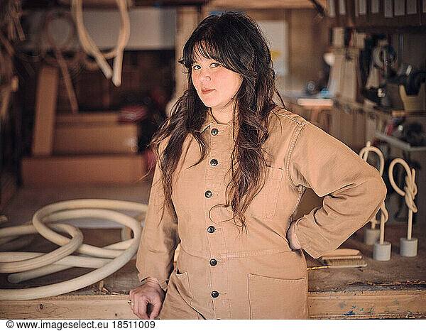 A female artist poses in her woodshop studio in front of her work