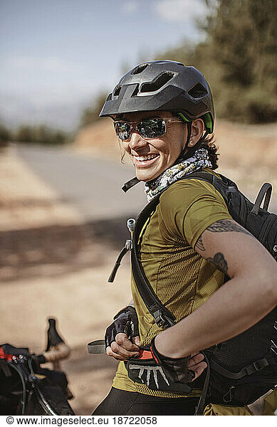 A female cyclist wearing sunglasses smiles while stopped on the road