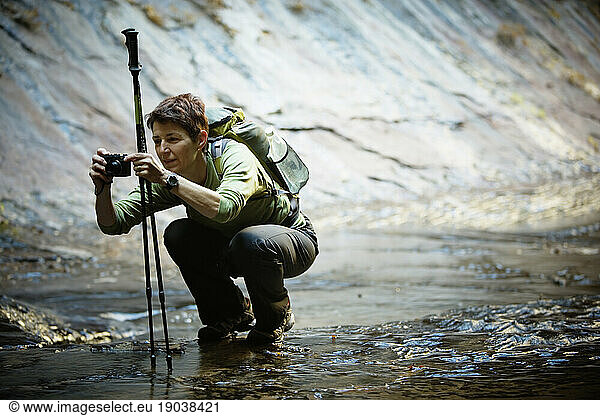 A female hiker squatting down  taking a photograph in Left Fork of North Creek  The Subway  Zion National Park  Utah.