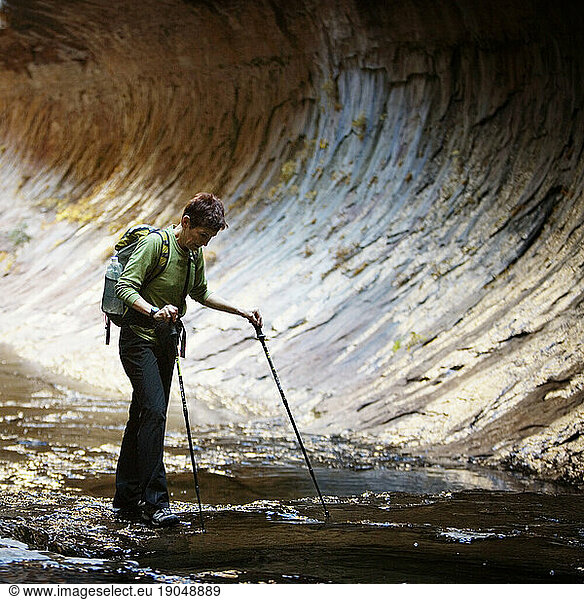 A female hiker with tekking poles  crossing the Left Fork of North Creek in The Subway in Zion National Park  Utah.
