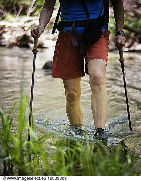 A female hikers legs and trekking poles while crossing a creek.