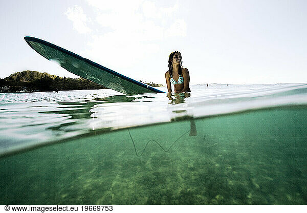 a female teen surfer sits on her surboard waiting on the next wave