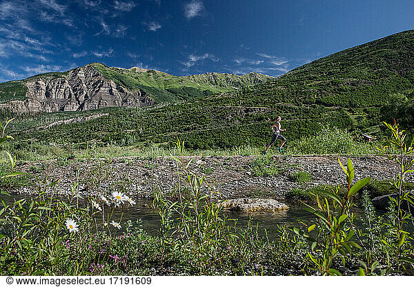 A female trail runner sprints along trail with river and mountains