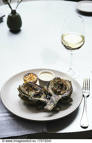 A fire roasted artichoke paired with a glass of white wine.