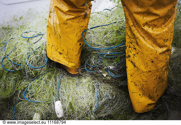 A fisherman in waders  standing on heaps of fishing nets.