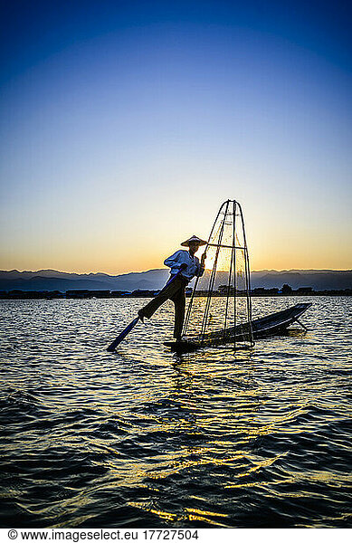 A fisherman on his boat on Lake Inle standing using his leg to move the oar.