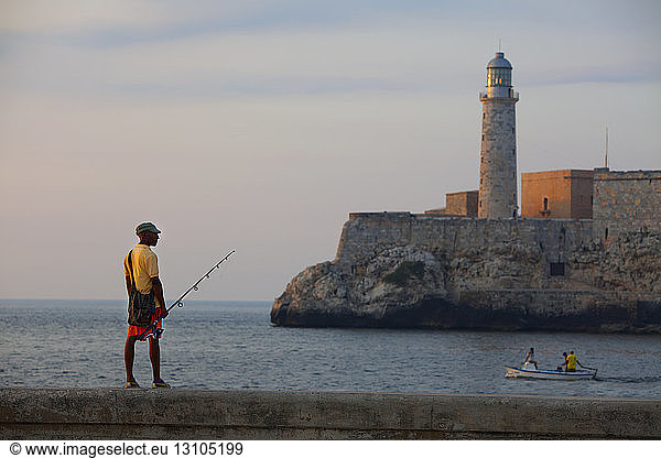 A fisherman standing on the railing on the Malecon harbour wall at the entrance to the harbor in Havana  Cuba.