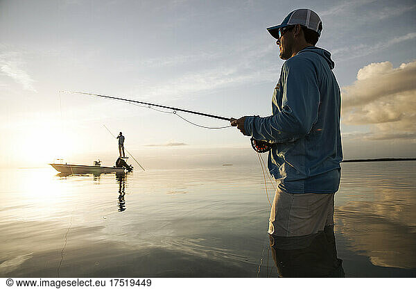 A fisherman wades while fly fishing in keys with boat in background