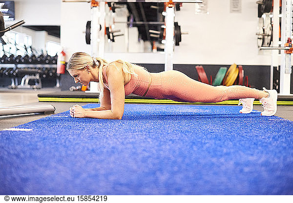 A fit female doing a forearm plank in the gym.