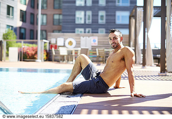 A fit man relaxes by the pool.