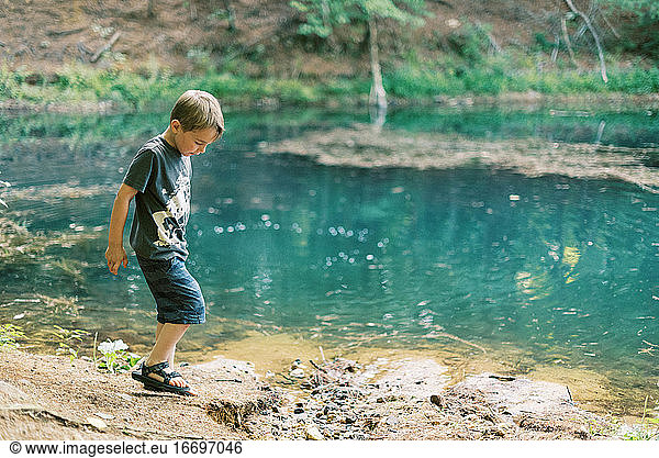 A five year old boy playing by a turquoise pond in the woods
