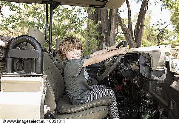 A five year old boy seated in the driving seat of a safari jeep pretending to drive.