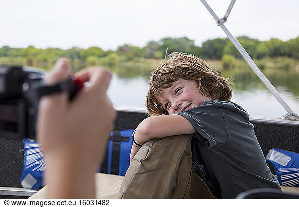 A five year old boy smiling at the camera on a river boat on the Zambezi River.